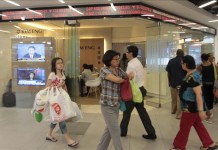 Clientes de un centro comercial pasan junto a una pantalla que muestra resultados de la Bolsa de Singapur. Archivo